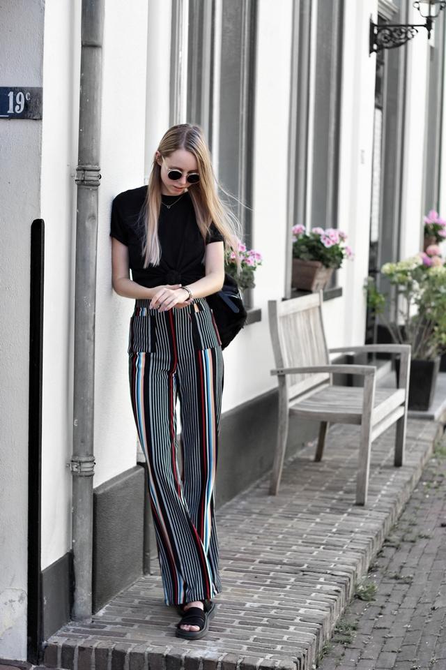 Outfit met wijde gestreepte palazzo broek en Gold Bandits armband witgoud bedel transparante polette zonnebril fluffy zachte Stradivarius rugzak Dr. Martens sandalen